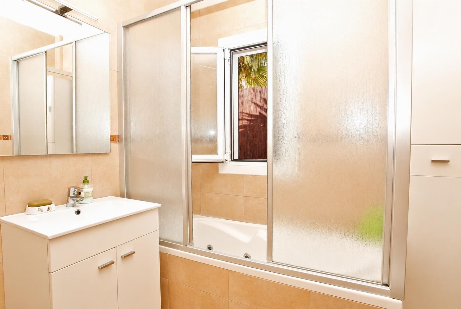 Een badkamer met een witte wastafel, spiegel en douchecabine met gesatineerd glazen deuren.