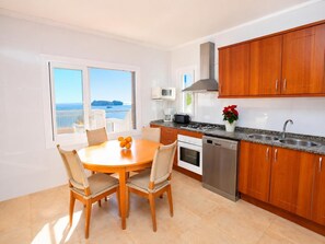 A modern kitchen with wooden cabinets, a dining table with chairs, a view of the sea, and a balcony. - Villa Maria de Bonaire (Mallorca)