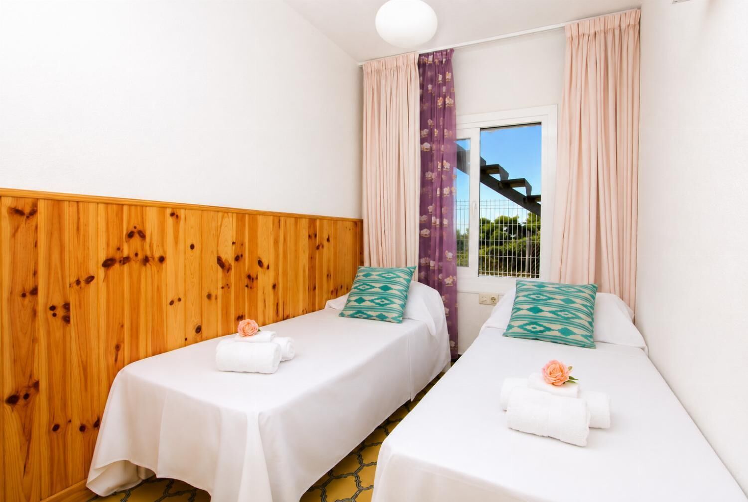 Een hotelkamer met twee enkele bedden, houten lambrisering aan een wand en een raam met gordijnen.