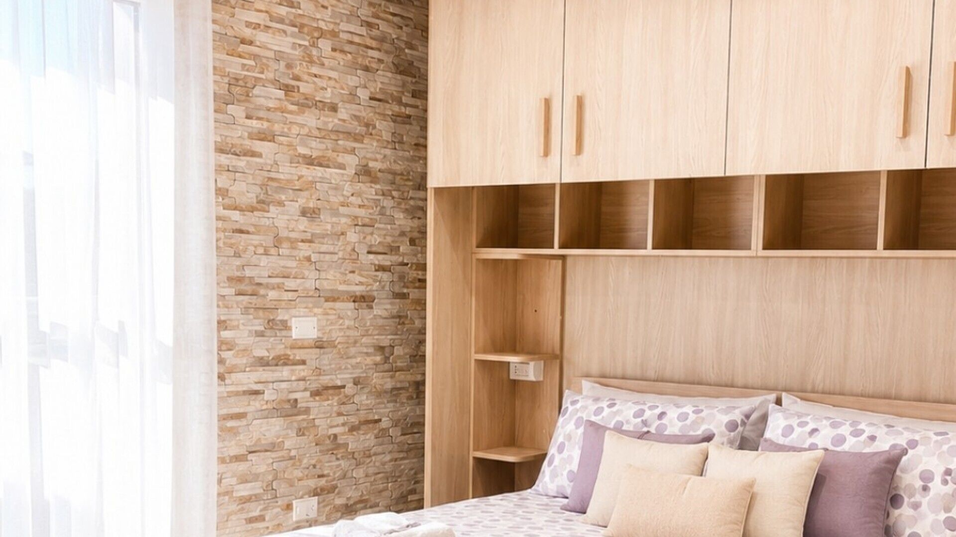 A bedroom with a bed, a wooden wardrobe, and a brick wall.