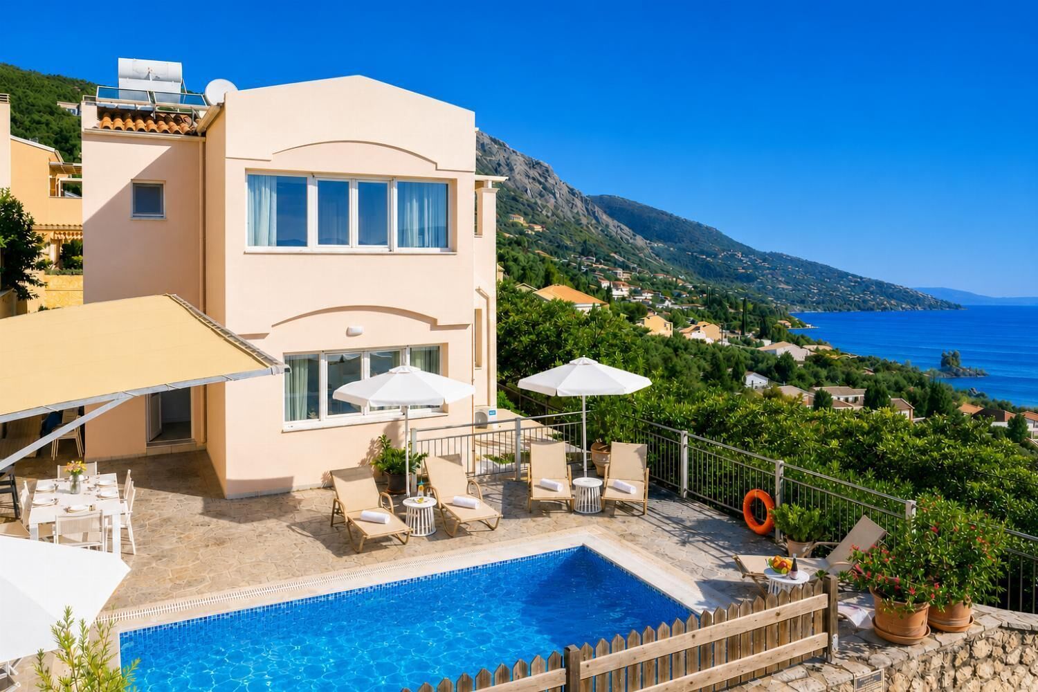 Un edificio de dos pisos con piscina, mobiliario exterior y vistas al mar y las colinas.