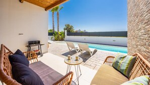 A covered outdoor area with wicker furniture, a pool, and a view of the sea.
