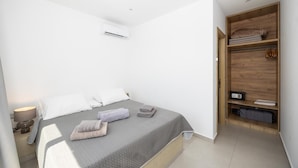 A bedroom with a bed, a bedside table, a lamp, a wardrobe, and an air conditioning unit.