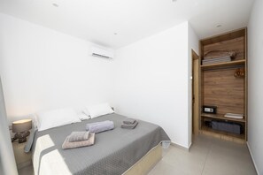 A bedroom with a bed, a bedside table, a lamp, a wardrobe, and an air conditioning unit. - Villa Salty Sun 5 - Two Bedroom Villa, Sleeps 4 (Kremasti)