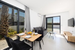 A modern living room with a dining area, a sofa, a TV, and a balcony with a view. - Villa Salty Sun 5 - Two Bedroom Villa, Sleeps 4 (Kremasti)