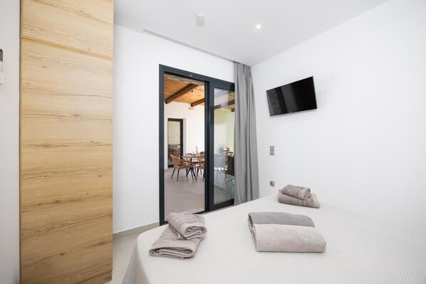 Una camera d'albergo moderna con una porta in legno, un letto con due asciugamani, una televisione a schermo piatto e vista sulla sala da pranzo attraverso una porta in vetro.