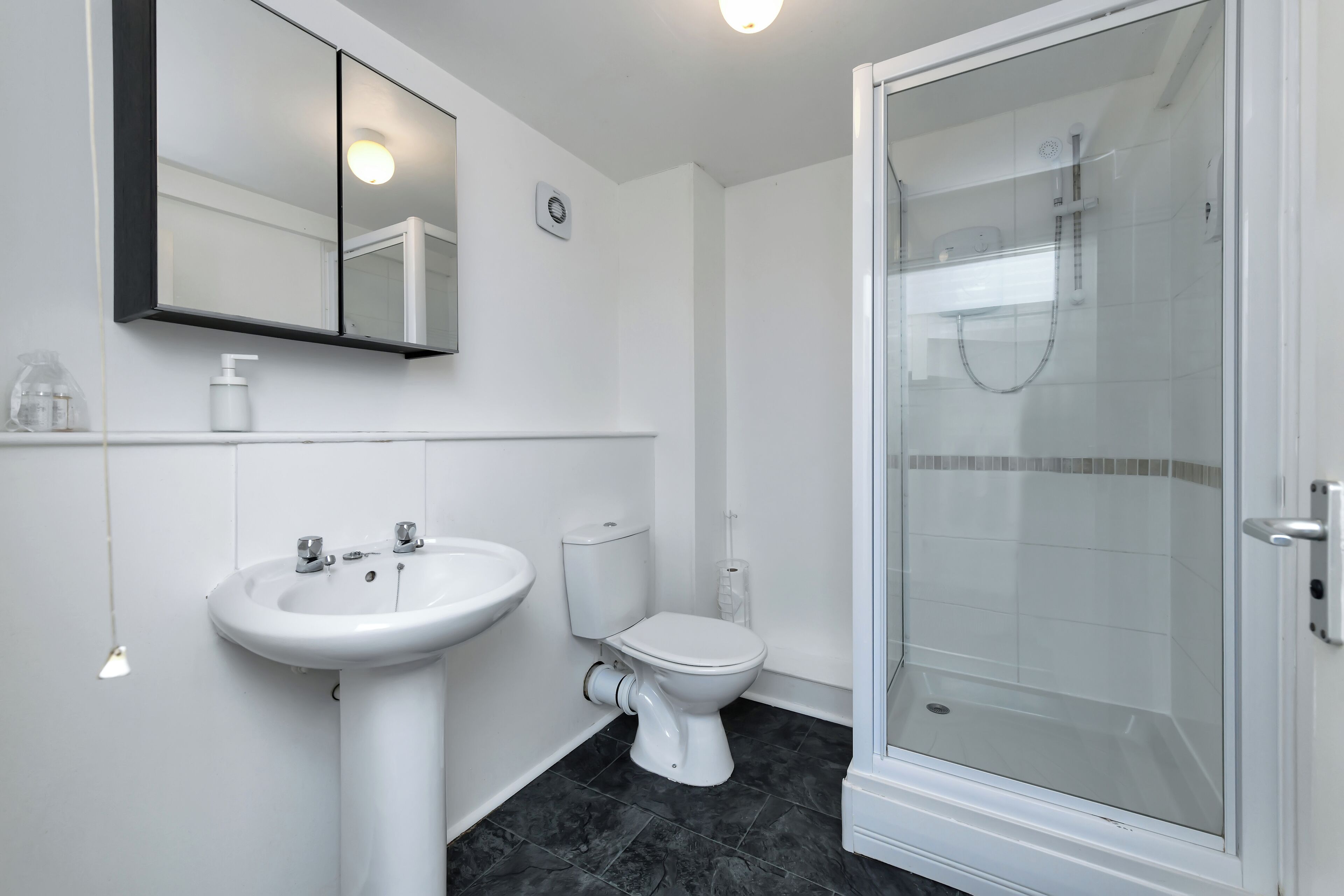 A modern bathroom with a white sink, toilet, and glass-enclosed shower.