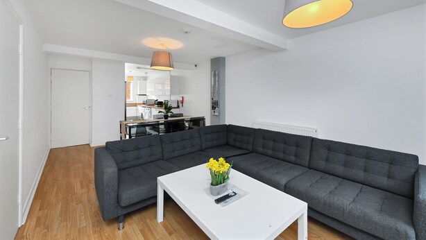 Ein modernes Wohnzimmer mit einem grauen Ecksofa, einem weißen Couchtisch mit Blumenvase und Pendelleuchten.