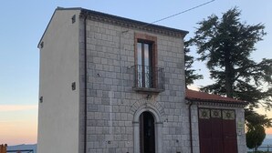 Edifici de dues plantes amb un balcó, una entrada ampla d'arc i una porta vermella.