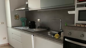 Una cuina moderna amb armaris blancs, una campana extractora d'acer inoxidable, un microones i un forn integrat.