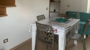 Zona de menjador amb escala de fusta, taula blanca i cadires.