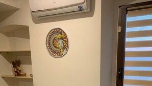 Un sofà de color verd mar amb una funda estampada, un aire condicionat fixat a la paret, una obra d'art circular decorativa i una finestra amb persianes.