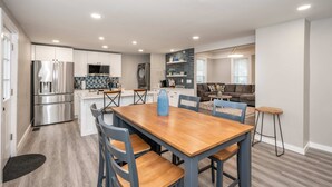 Eine moderne Küche mit Edelstahlgeräten, ein Essbereich mit Holztisch und blauen Stühlen sowie ein Wohnzimmer mit Sofa und Couchtisch.