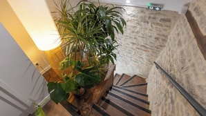 A staircase with a wooden handrail, a potted plant, and a wall with a stone texture. - Hotel les Vents d'Anges (Beaune)
