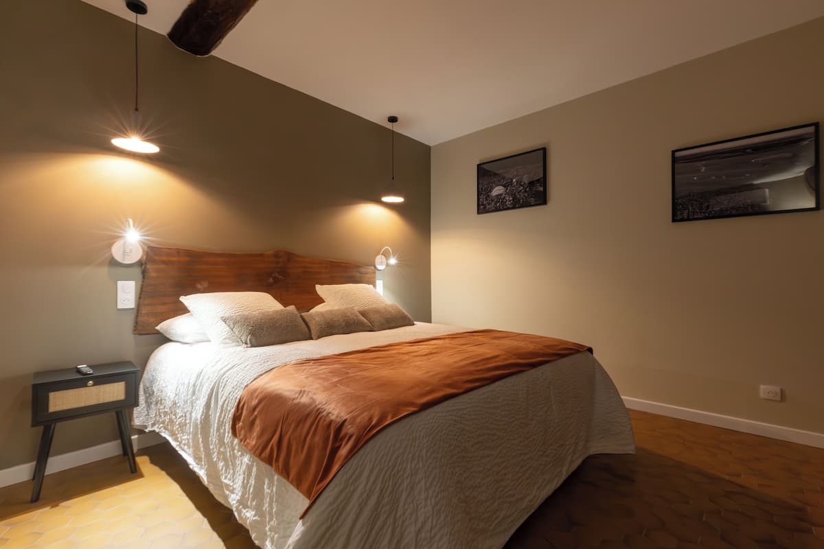 Quarto com cama grande, duas luzes na parede, mesa de cabeceira e duas fotos emolduradas.