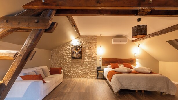 A cozy attic bedroom with a loft bed, a sofa, and a stone wall. - Hotel les Vents d'Anges (Beaune)