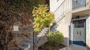 A stone wall with a vine-covered section, a small tree, and a door with a letter 'H'. - Hotel les Vents d'Anges (Beaune)
