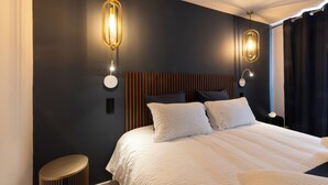 A modern bedroom with a large bed, two bedside tables, and a wall-mounted light fixture. - Hotel les Vents d'Anges (Beaune)