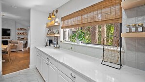 Una cocina moderna con armarios blancos, encimera de mármol, una ventana con persiana de bambú y una estantería metálica negra.