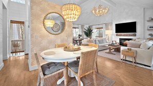 Amplia sala de estar con una mesa de comedor, dos candelabros, una chimenea y un televisor grande montado en la pared.