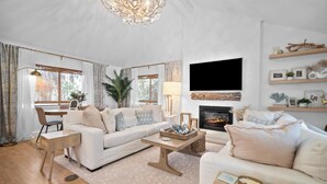 Un salón espacioso con chimenea, un conjunto de sofás, una mesa de centro y un televisor montado en la pared.