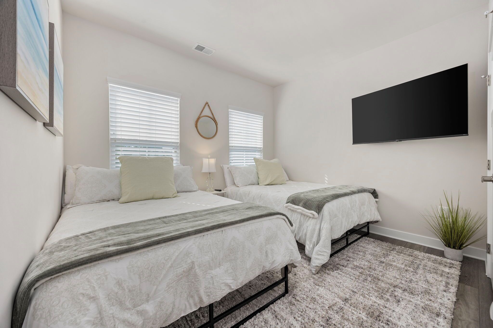 A bedroom with two beds, a flat-screen TV, and a potted plant.