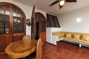 A dining area with a wooden table and chairs, a sofa, and a ceiling fan. - Villas el Parque #18B: Central Studio Apartment, Pool, AC, WiFi & Wildlife (Quepos)