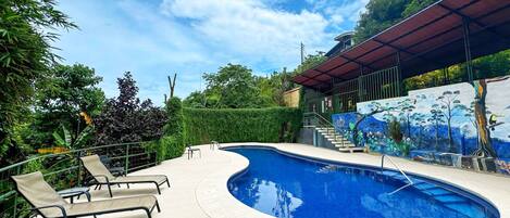 A swimming pool with lounge chairs, surrounded by greenery and a mural.