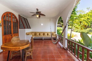 A covered patio with a wooden table and chairs, a sofa, a hammock, and a ceiling fan. - Villas el Parque #18B: Central Studio Apartment, Pool, AC, WiFi & Wildlife (Quepos)