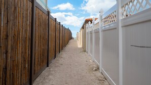 Un étroit sentier bordé de clôtures en bois et blanches, qui mène à un bâtiment doté d’un toit en tuiles.