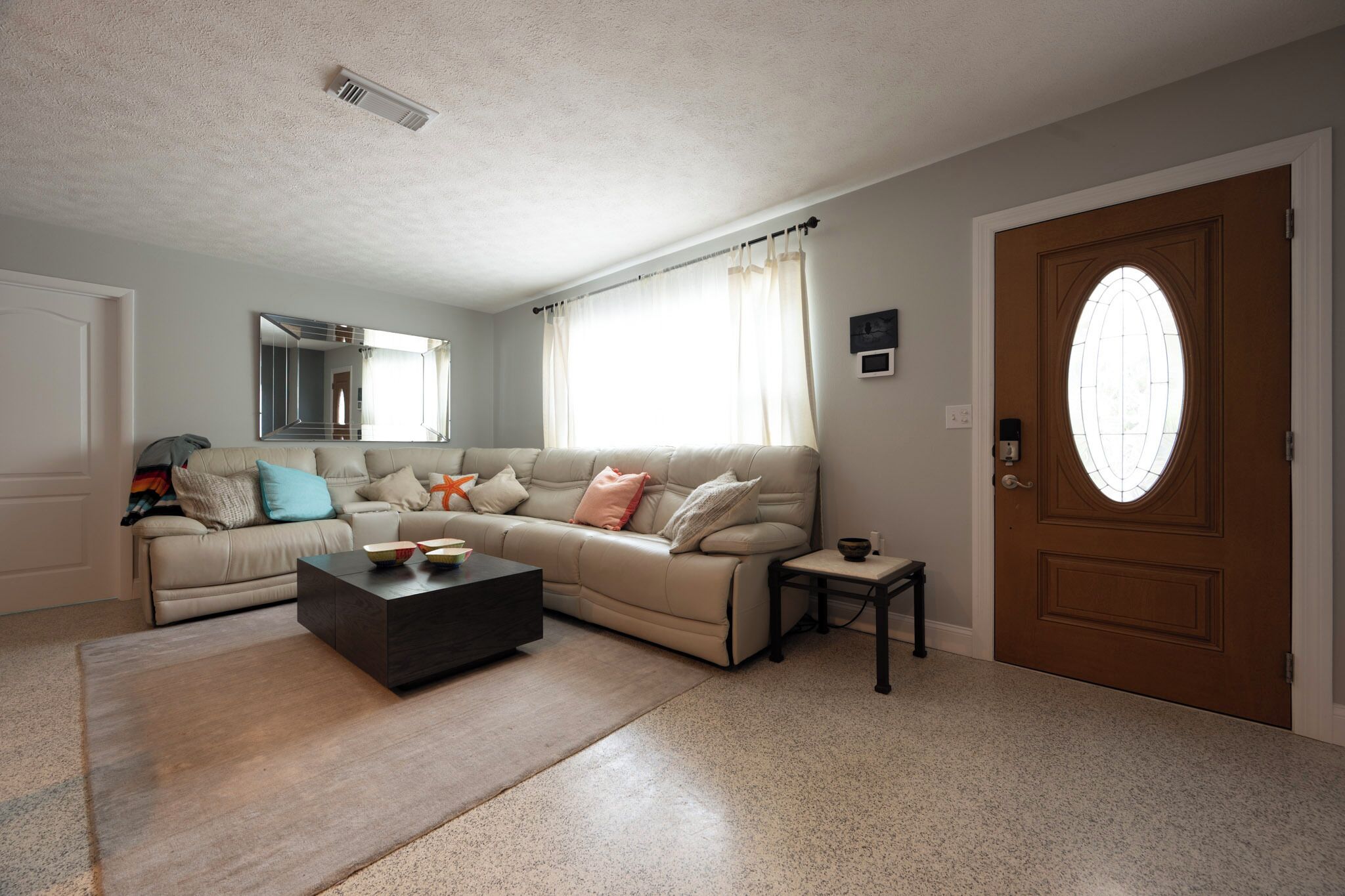 Una sala de estar con un sofá color beige, una mesa de centro y una puerta con ventanal.