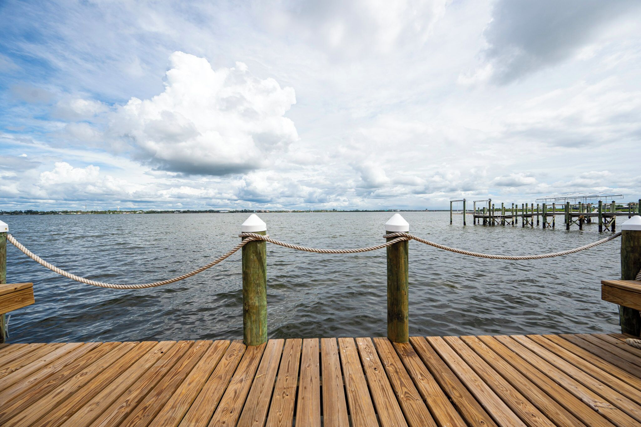 A wooden dock extending into calm water with a rope barrier and a cloudy sky.