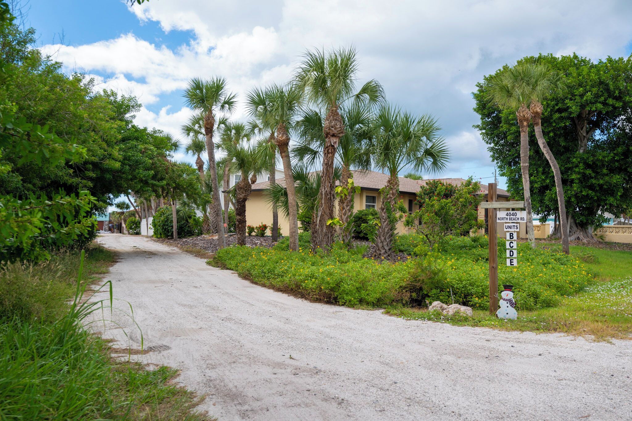 A dirt road leading to a residential area with palm trees and a sign indicating 'NORTH BEACH RD. 4040 UNITS B C D E'.