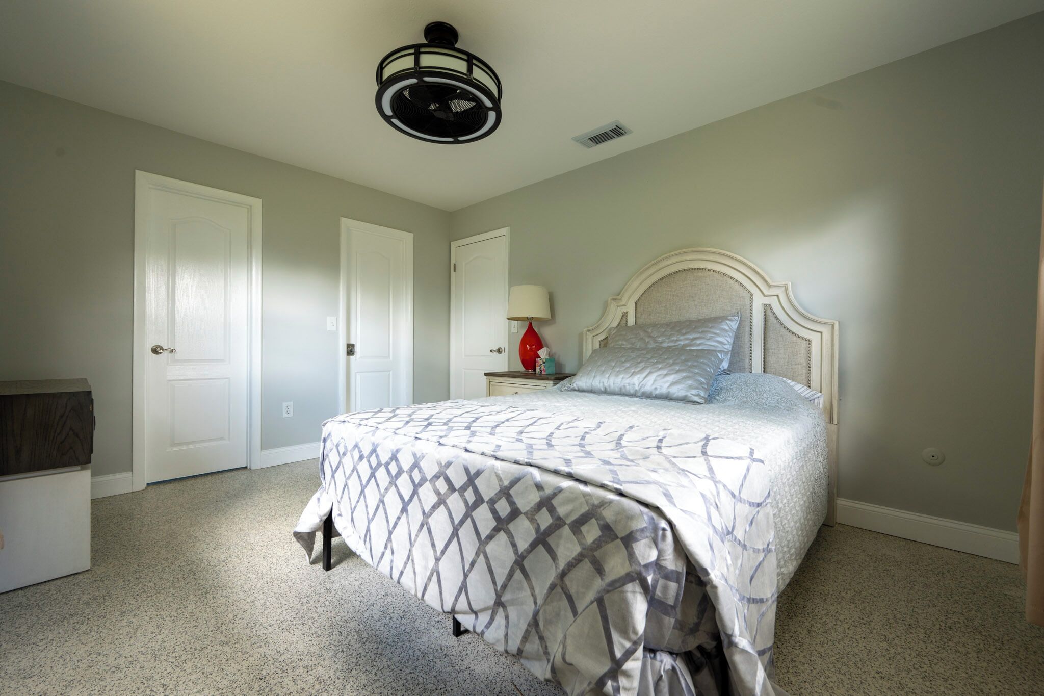 Une chambre à coucher avec un lit, une table de chevet avec une lampe et un ventilateur de plafond.