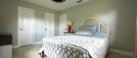 A bedroom with a bed, a nightstand with a lamp, and a ceiling fan.