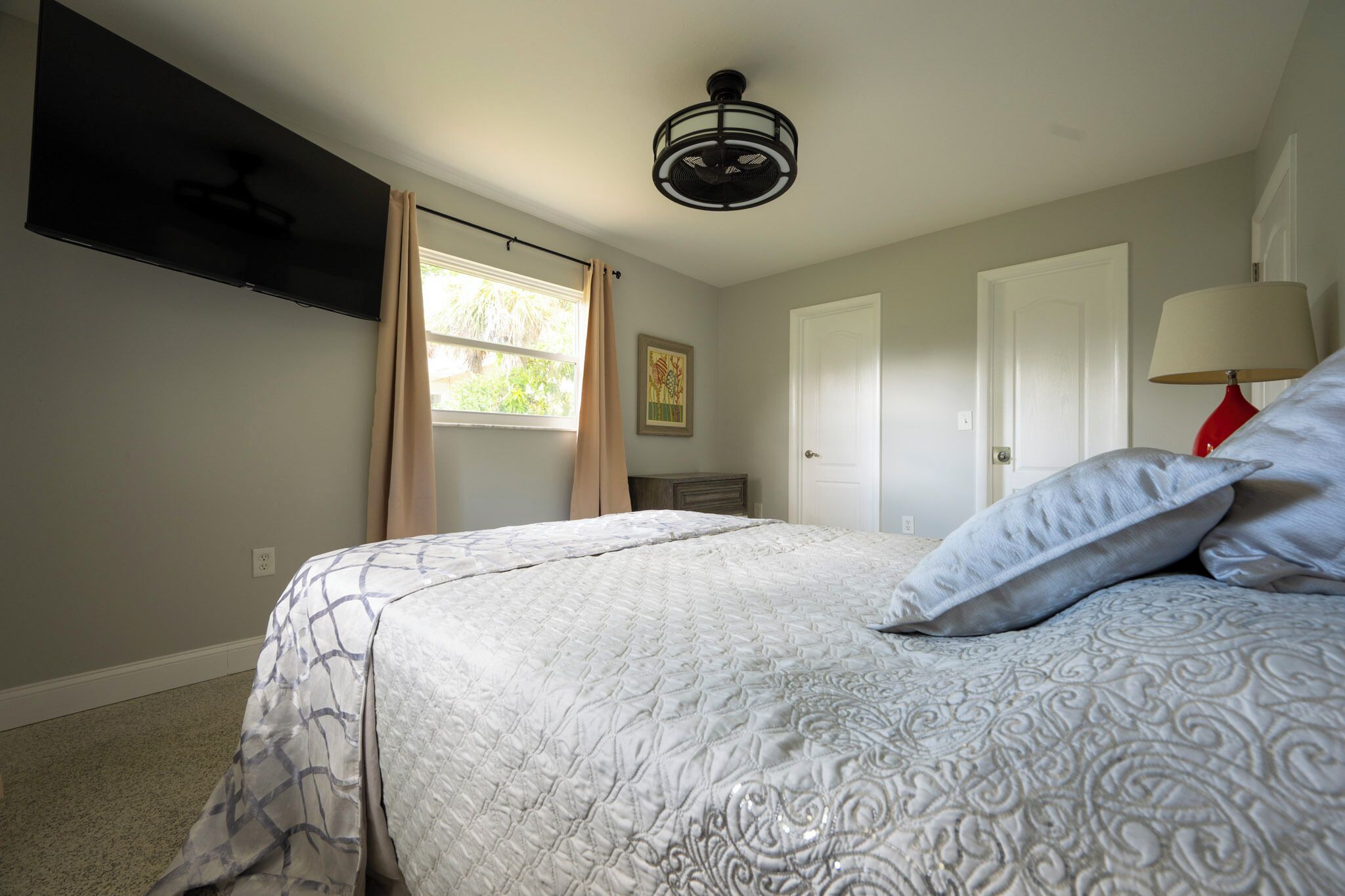 Ein Schlafzimmer mit Bett, Deckenventilator, Fenster mit Vorhängen und einer Tür.