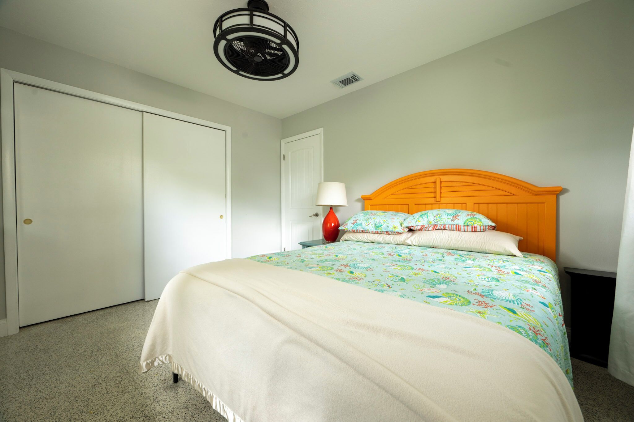 Une chambre à coucher avec un lit, une table de chevet, une lampe et un ventilateur de plafond.