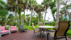 Une terrasse en bois, agréée de mobilier d’extérieur, notamment une table et des chaises, entourée de palmiers et de verdure.