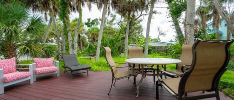 A wooden deck with outdoor furniture, including a table and chairs, surrounded by palm trees and greenery.