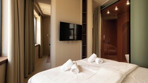 A hotel room with a bed, a flat-screen TV mounted on the wall, a shower area, and a walk-in closet. - Boutique Hotel OPERA (Rijeka)