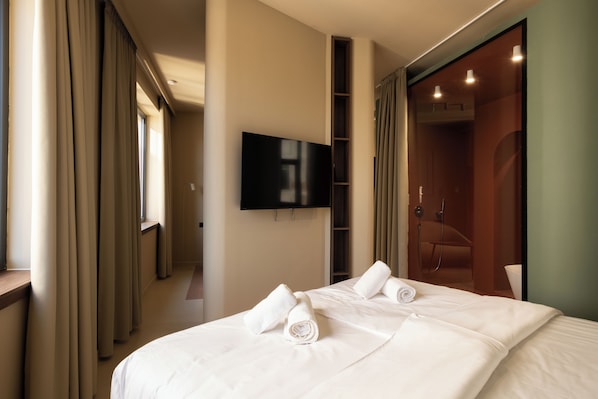 Une chambre d’hôtel comprenant un lit, un téléviseur à écran plat fixé au mur, un espace douche et un dressing.