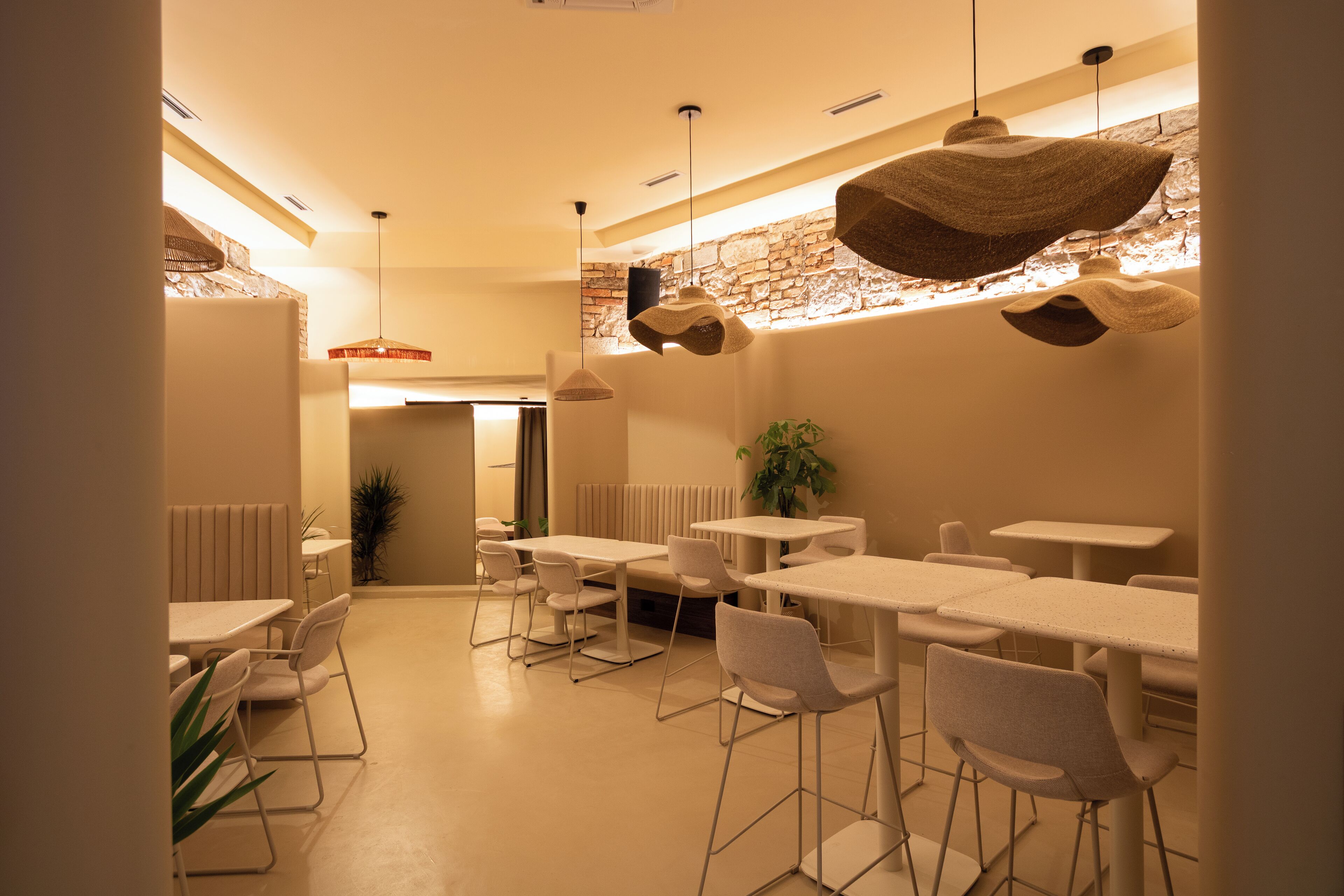 A modern dining area with white tables and chairs, a stone accent wall, and hanging pendant lights.