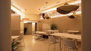 A modern dining area with white tables and chairs, a stone accent wall, and hanging pendant lights.