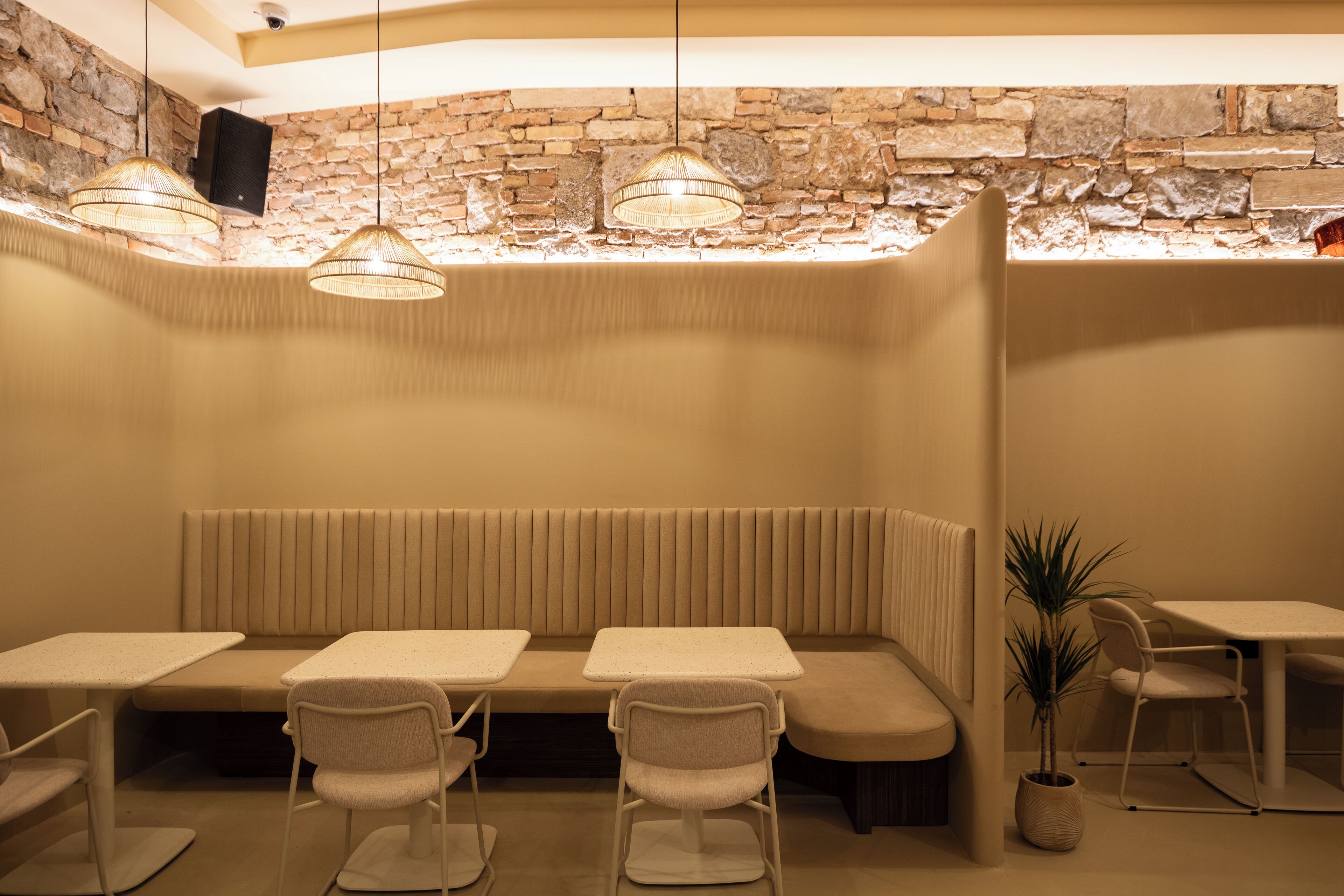 A cozy restaurant with a stone wall, cushioned seating, and pendant lighting.
