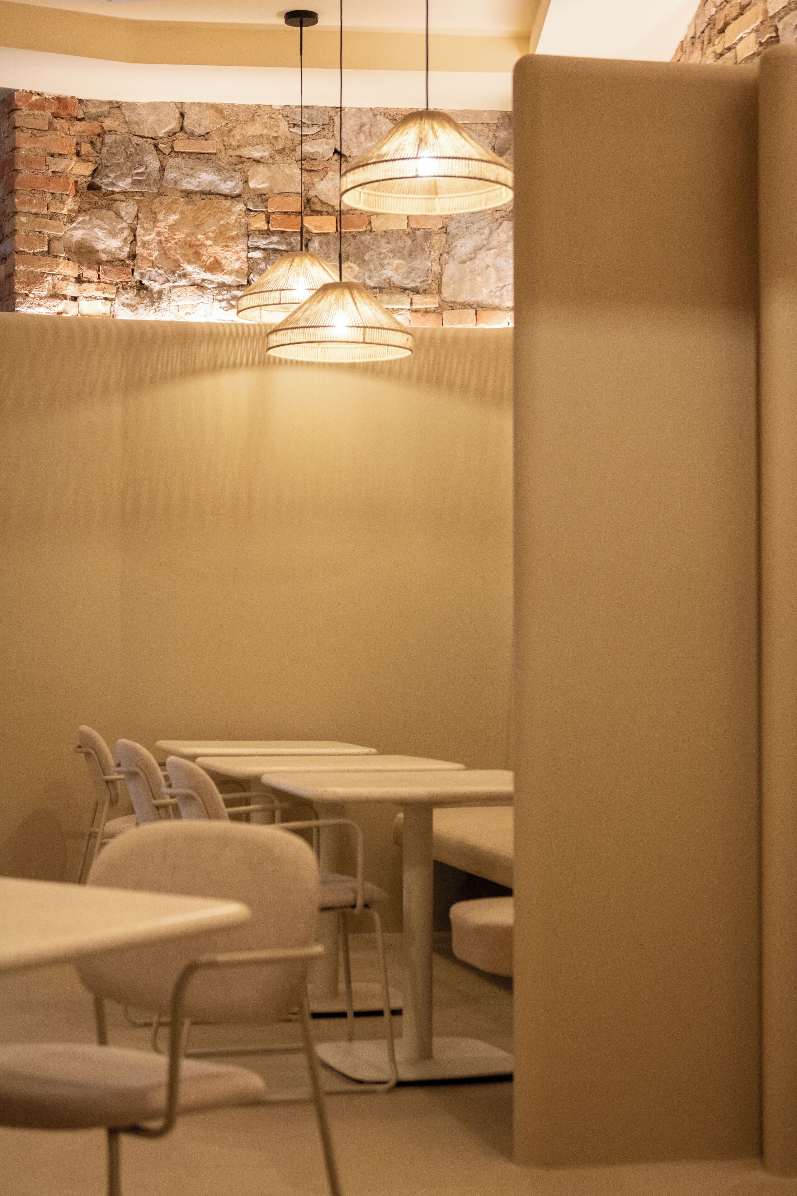 A dining area with tables and chairs, a stone wall, and hanging lamps.