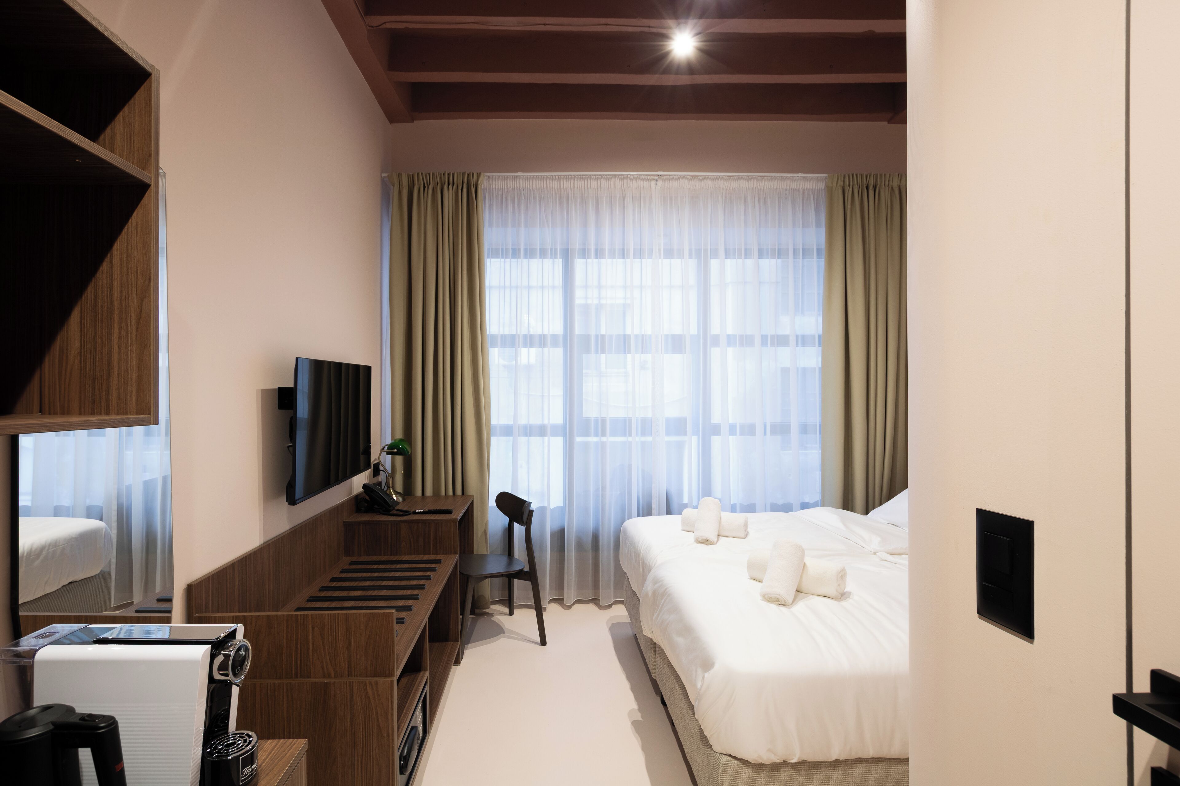 A hotel room with a bed, a desk with a chair, a television, and a window with curtains.