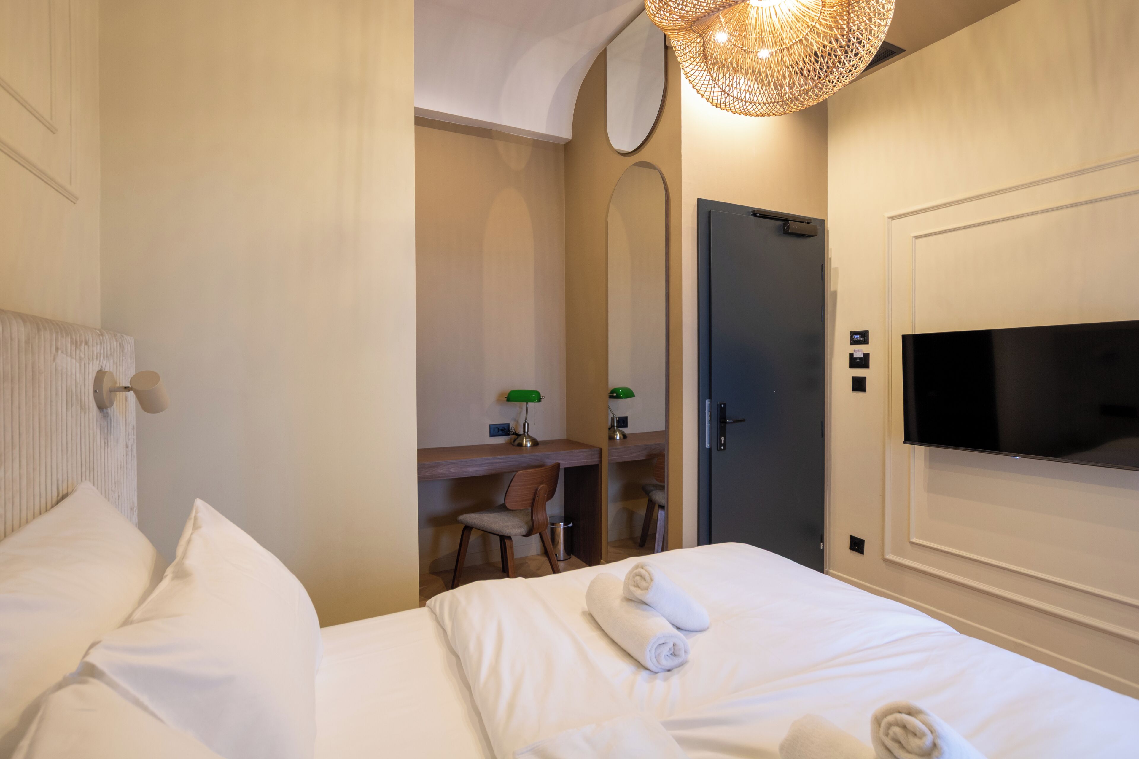 A hotel room with a bed, a desk with a chair, a television, and a door.