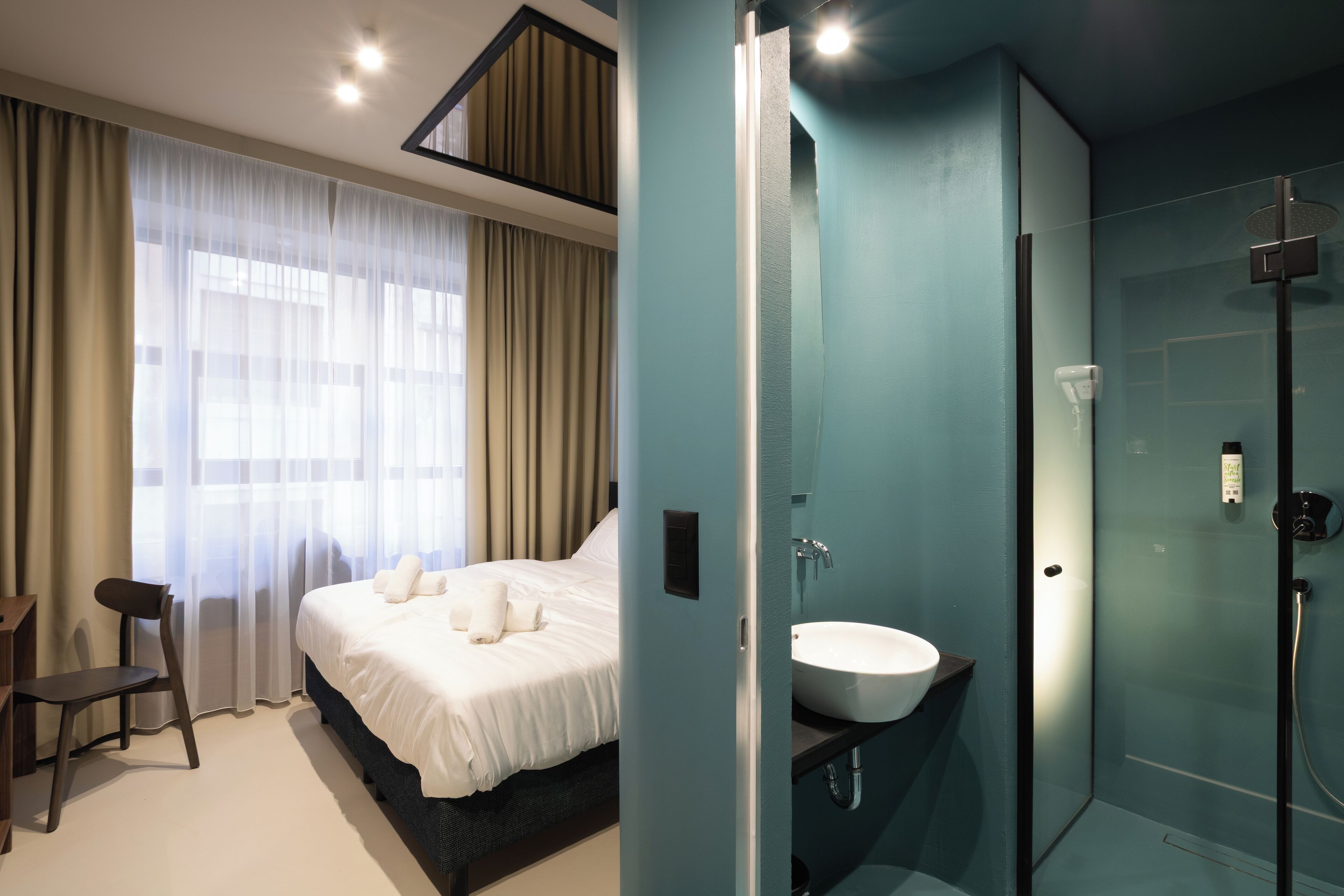Une chambre d’hôtel moderne dotée d’un grand lit, d’une table de chevet, d’une chaise et d’une salle de bain avec une douche à parois de verre.