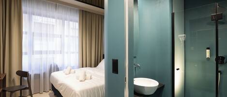 Une chambre d’hôtel moderne dotée d’un grand lit, d’une table de chevet, d’une chaise et d’une salle de bain avec une douche à parois de verre.