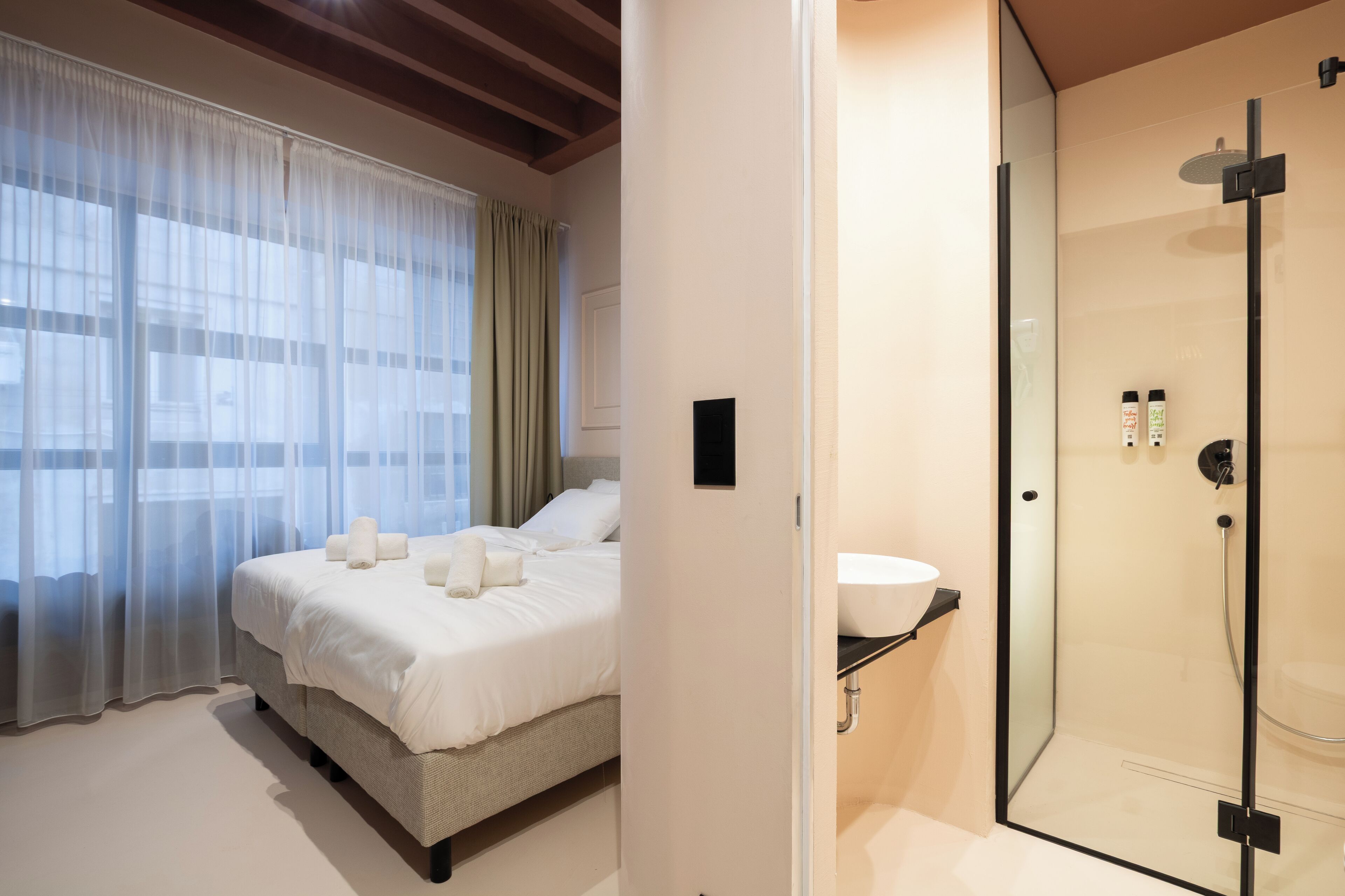 A hotel room with a bed, a shower, and a window with curtains.